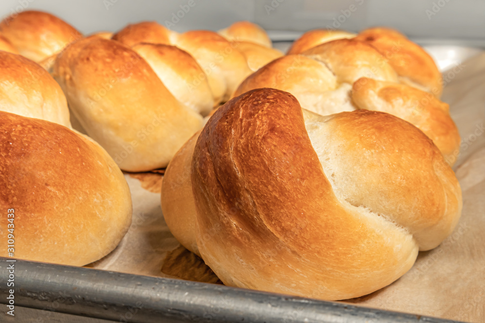 Homemade yeast buns tied up in a knot. Traditional Swiss bread recipe called Zopf or Butterzopf. The bread knots are arranged in rows on baking paper, fresh out off the oven. Homemade yeast buns tied up in a knot. Traditional Swiss bread recipe called Zopf or Butterzopf. The bread knots are arranged in rows on baking paper, fresh out off the oven.