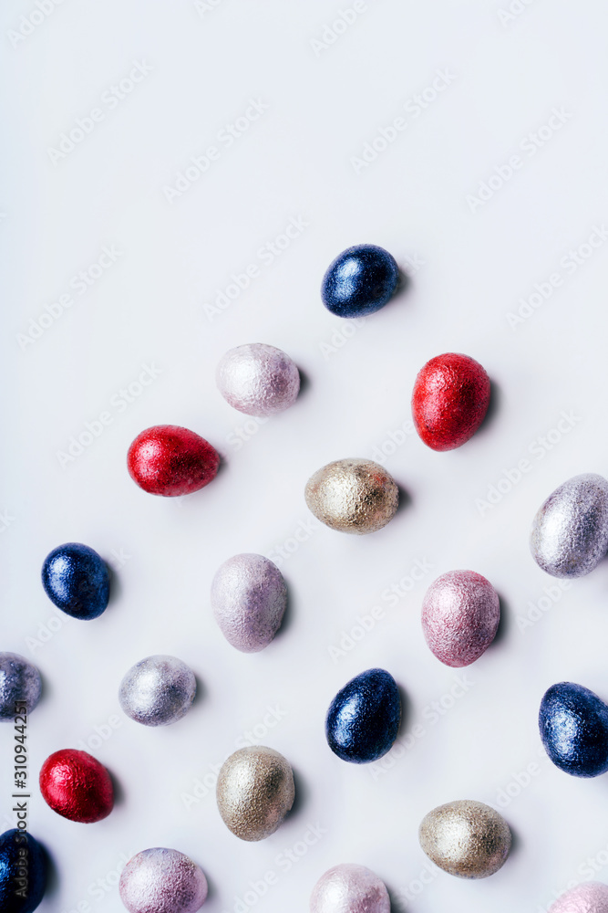 Colored painted pearl chicken and quail eggs pink, silver, golden and blue color on a light blue pastel vertical background. Minimalistic creative classic easter festive flat lay. Copyspace for text