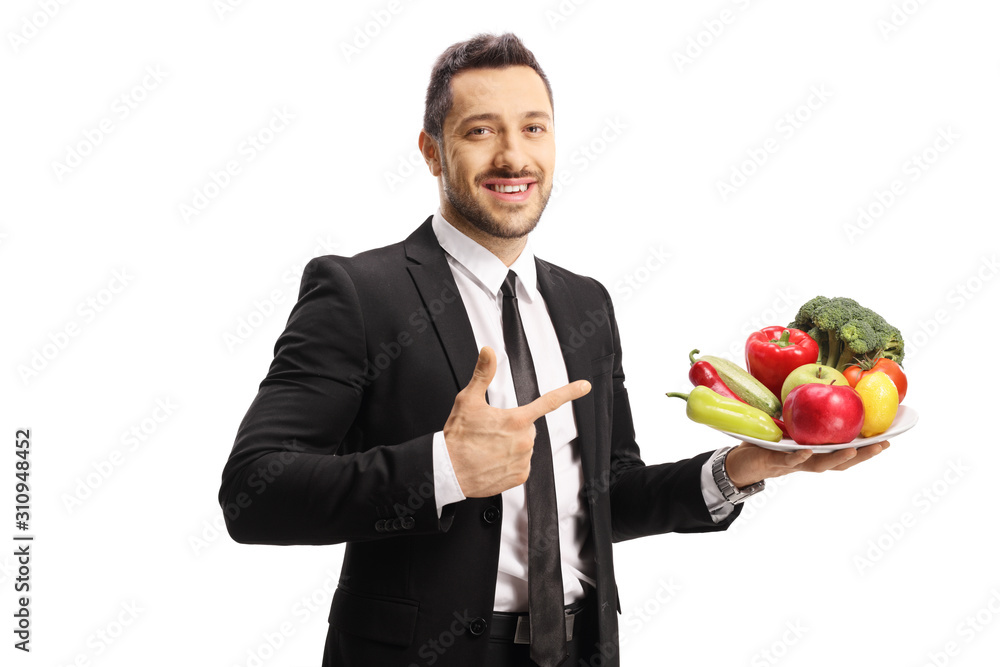 Young man in a suit holding a plate of fruits and vegetables and pointing Young man in a suit holding a plate of fruits and vegetables and pointing