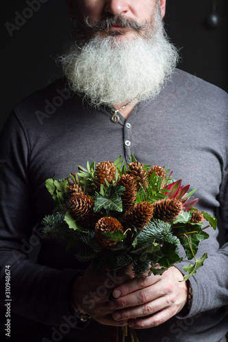 Middle-aged bearded man holding a winter bouquet of Nobil fir twigs, cones, pistachio, leucodendron and ivy, winter gift concept photo