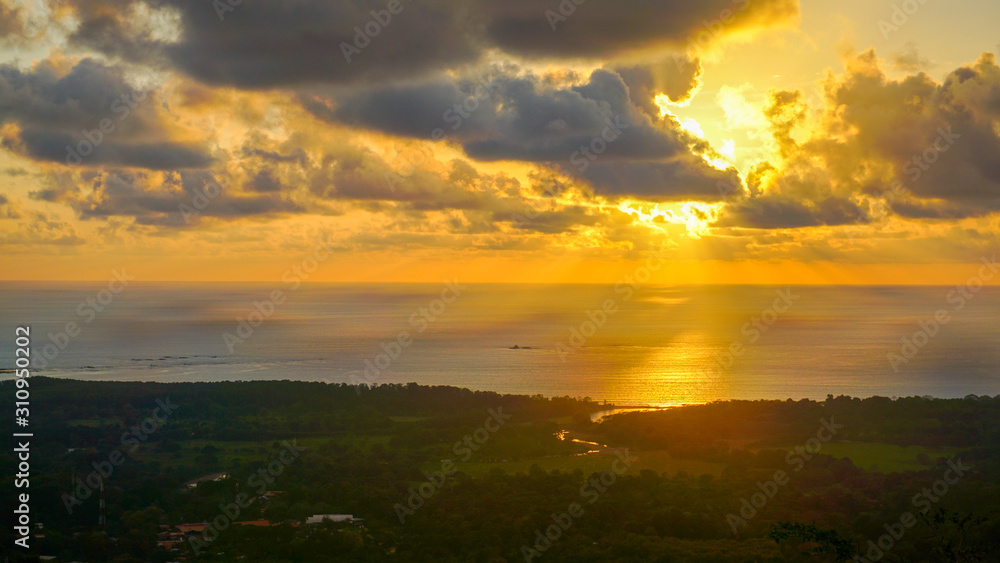 Spectacular sunset over the pacific while the sun's rays are breaking through the clouds over the ocean and the mainland. Amazing view over the jungle and the ocean with many tone colours on the sky.