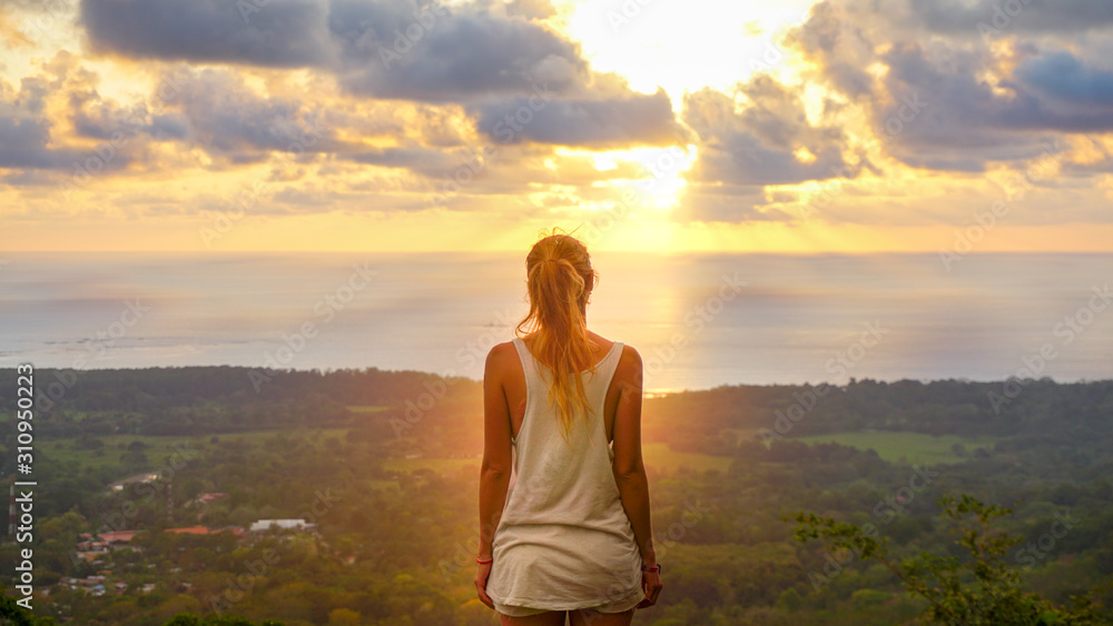 Inspiring scene of a woman standing at the viewpoint looking straight towards the pacific ocean during a stunning sunset making sky colourful and sun rays braking true the clouds. Feeling the freedom. Inspiring scene of a woman standing at the viewpoint looking straight towards the pacific ocean during a stunning sunset making sky colourful and sun rays braking true the clouds. Feeling the freedom.