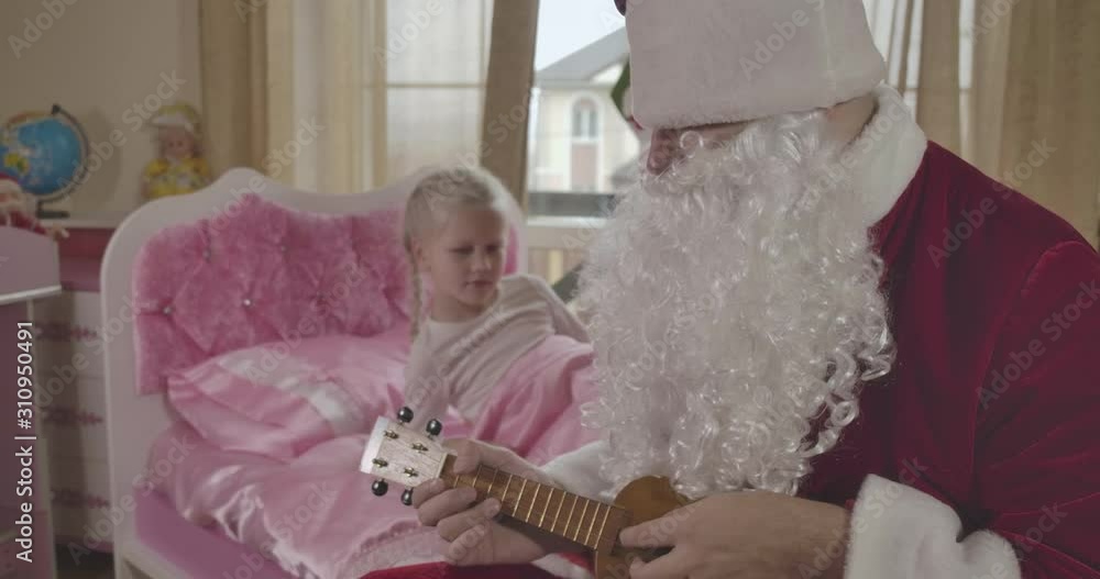 Blurred Caucasian girl waking up in the morning and seeing Santa Claus sitting on her pink bed and playing ukulele. Father surprising daughter on Christmas eve. Cinema 4k ProRes HQ. Blurred Caucasian girl waking up in the morning and seeing Santa Claus sitting on her pink bed and playing ukulele. Father surprising daughter on Christmas eve. Cinema 4k ProRes HQ.