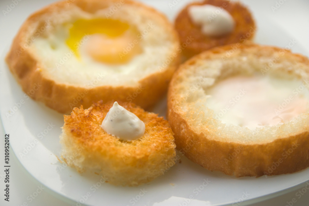 fried eggs baked in round bread with croutons on a white plate top view  close up