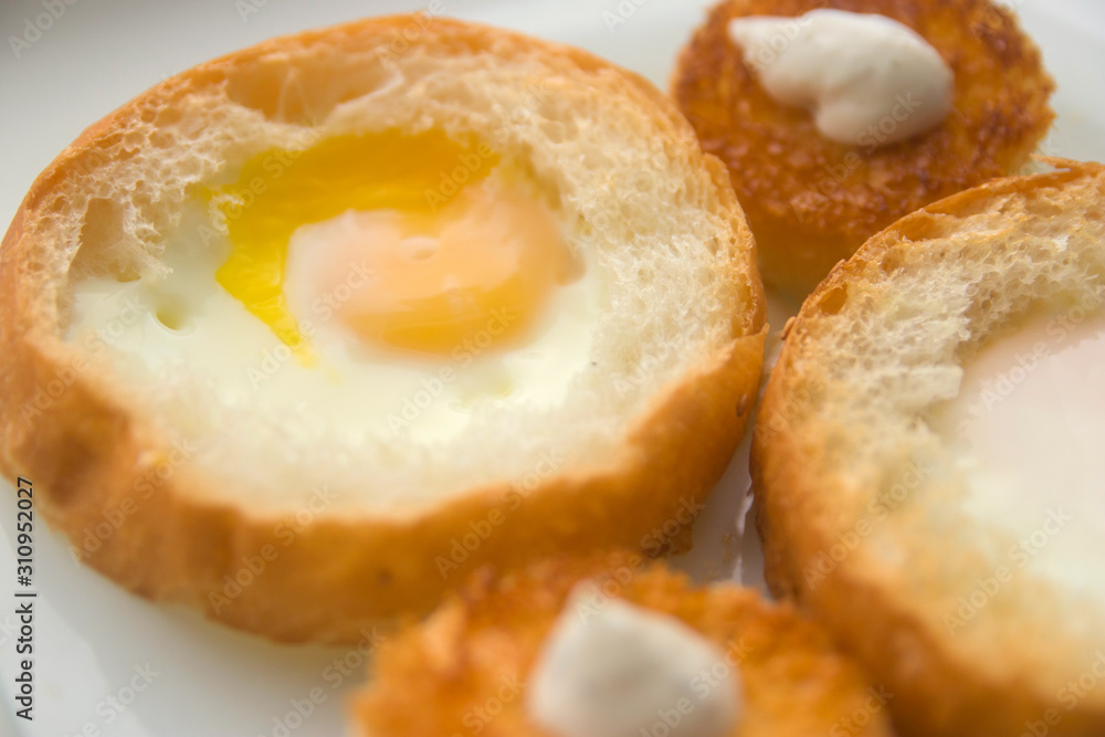 fried eggs baked in round bread with croutons on a white plate top view close up