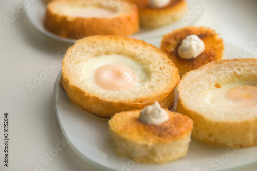 fried eggs baked in round bread with croutons on a white plate top view close up