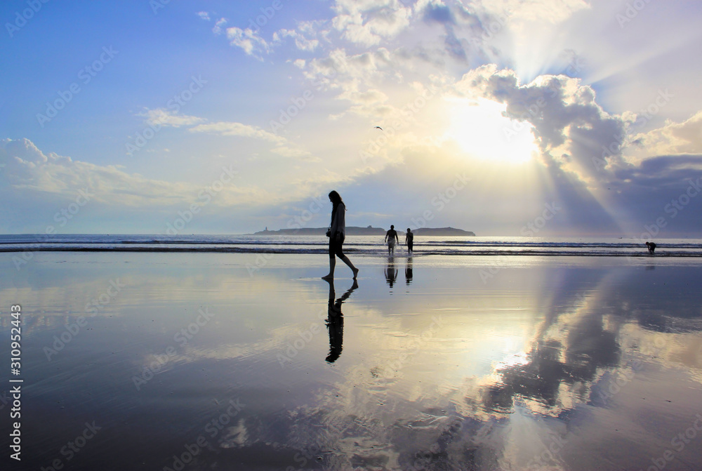 Girl walking on the beach turned into a mirror by the low tide. Sunset at the Essaouira, Morocco