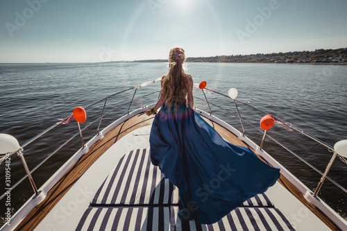 Woman in flying beautiful blue dress on a boat. Wide view on front of yacht. Back view © Ivan K.