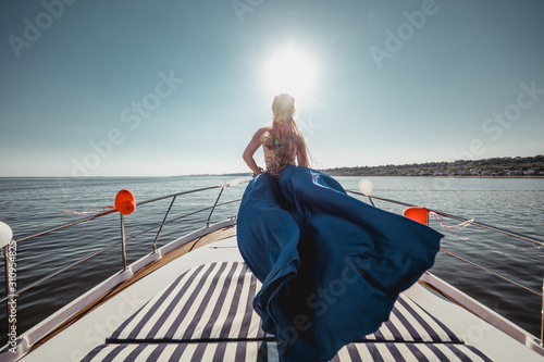 Woman in flying beautiful blue dress on a boat. Wide view on front of yacht. Back view © Ivan K.