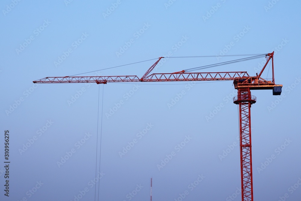 Red steel construction crane with building in city background and blue sky light sunset Red steel construction crane with building in city background and blue sky light sunset
