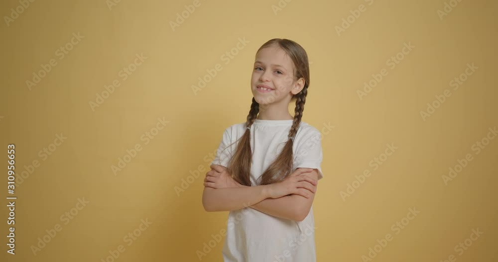 Little girl in white t-shirt crossing her arms at yellow background slow motion Little girl in white t-shirt crossing her arms at yellow background slow motion