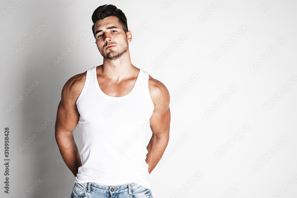 Handsome young man with stylish haircut in undershirt and jeans posing over grey background. Perfect hair & skin. Close up. Studio shot Handsome young man with stylish haircut in undershirt and jeans posing over grey background. Perfect hair & skin. Close up. Studio shot