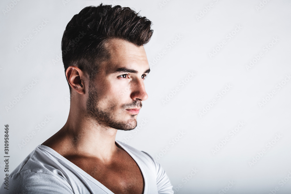 Obraz premium Male beauty concept. Portrait of handsome young man with stylish haircut posing over gray background. Perfect hair & skin. Close up. Studio shot