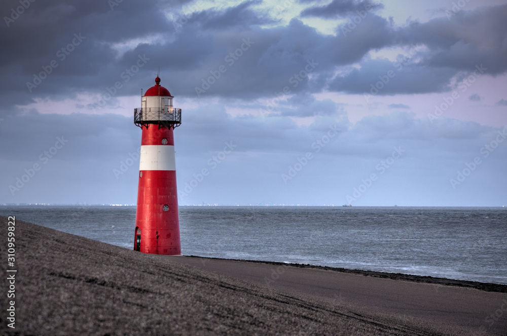 A red and white lighthouse at sea at dusk near Zeeland, Netherlands.