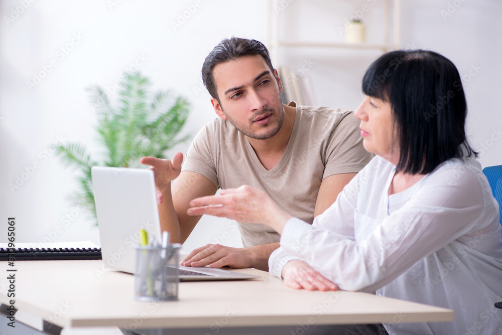 Young male employee explaining to old female colleague how to us Young male employee explaining to old female colleague how to us