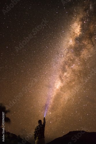 Silhouette of a young man with a torch shining on a milky way visible on a beach in Fiji