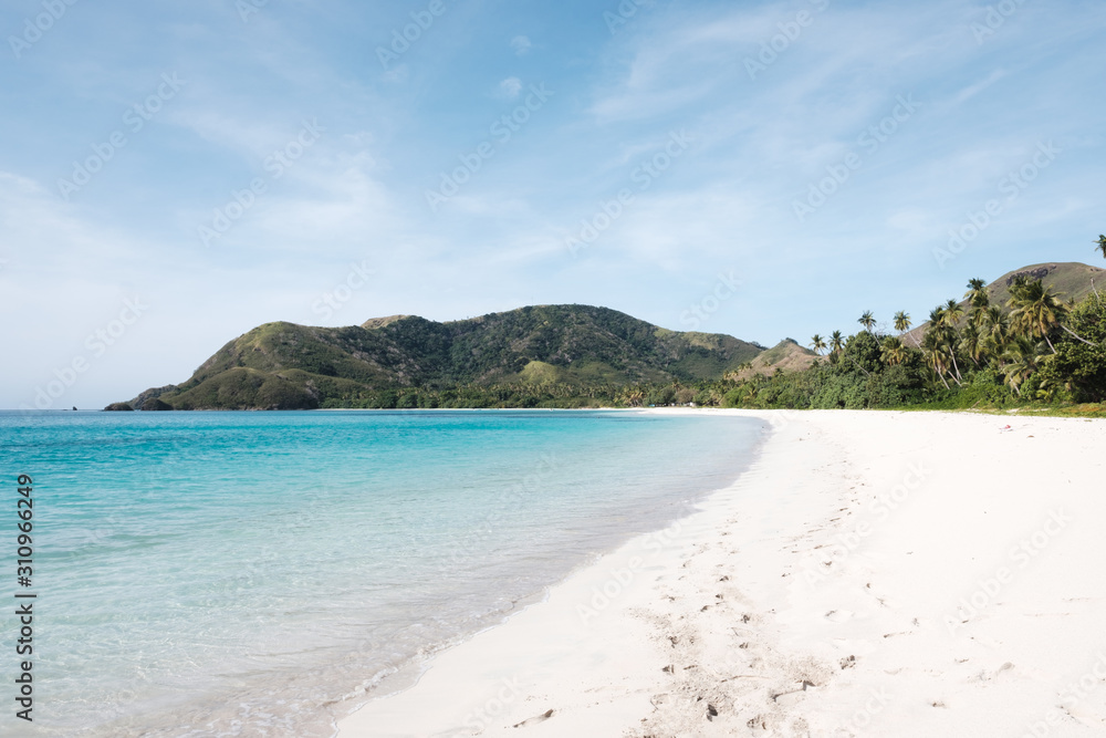 Beautiful white sandy beach in Fiji with turquoise water, green hills and plants, relaxing vacation destination
