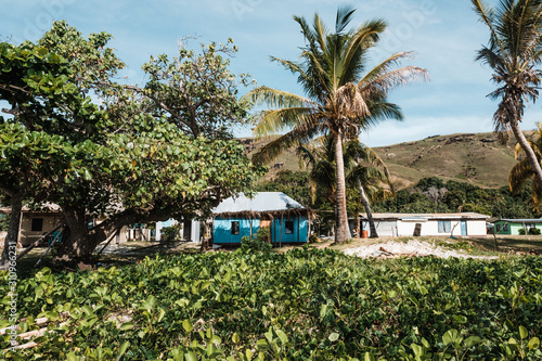 Malakati village, Fiji - 10/27/2019: Colourful house on the grass area on the beach with palm trees and green plants in traditional Fijian village during sunny day