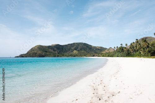 Beautiful white sandy beach in Fiji with turquoise water, green hills and plants, relaxing vacation destination © Klara