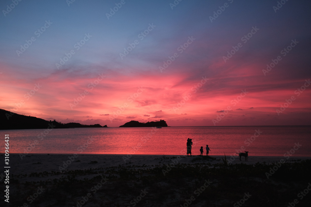 Malakati village, Fiji - 10/26/2019: Family walking on the beach, colourful sunset with palm trees over the ocean on a white sandy beach in Fiji Malakati village, Fiji - 10/26/2019: Family walking on the beach, colourful sunset with palm trees over the ocean on a white sandy beach in Fiji