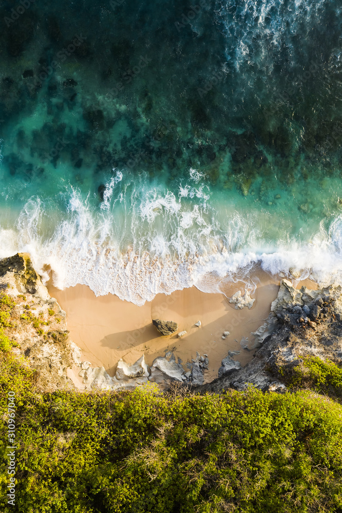 View from above, stunning aerial view of a rocky shore with a beautiful beach bathed by a rough sea during sunset, Nyang Nyang Beach (Pantai Nyang Nyang), South Bali, Indonesia.