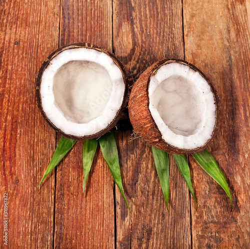 Pieces of coconut with fresh palm leaf on a wooden background. Top view.