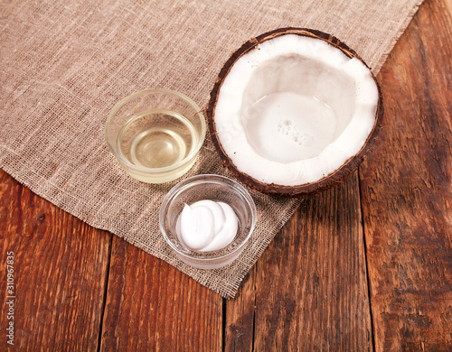 Coconut with cosmetic cream and coconut oil in the glass bowls on wooden background. 