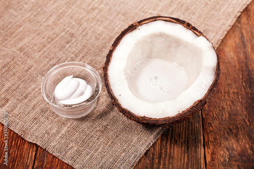 Coconut with cosmetic cream in glass bowl on wooden background. 