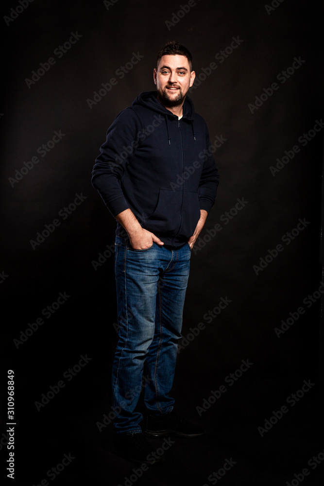 Handsome young man in jeans with a beard. Black background. Vertical. Handsome young man in jeans with a beard. Black background. Vertical.