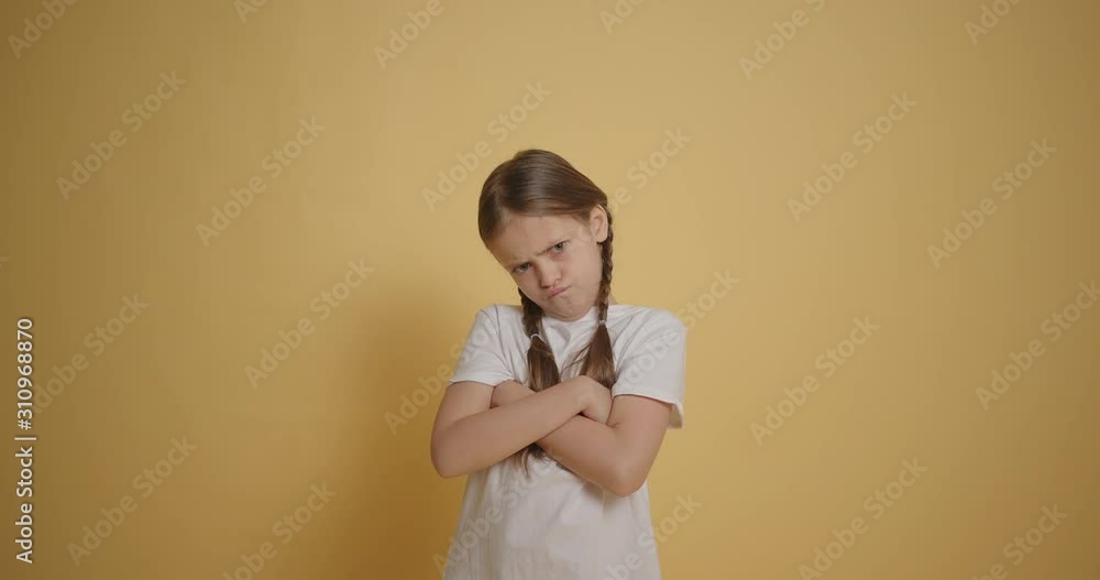Angry little girl looking seriously with crossed arms at yellow wall slow motion Angry little girl looking seriously with crossed arms at yellow wall slow motion