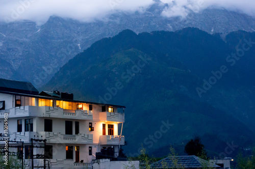 The warm lights from a building against the cool backdrop of fog covered mountains in the hill station of McLeodganj India © Memories Over Mocha