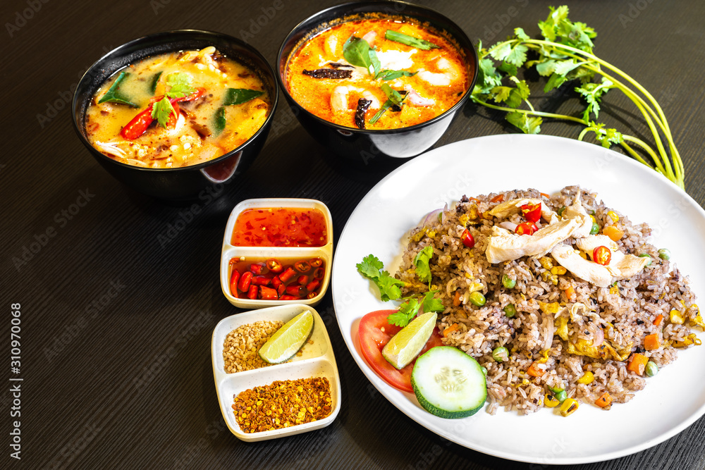 Thai olive fried rice served with prawns in a white plate, and two bowls of Tom Yum Soup in the background. Typical famous daily Thailand cuisine food on table. Thai olive fried rice served with prawns in a white plate, and two bowls of Tom Yum Soup in the background. Typical famous daily Thailand cuisine food on table.