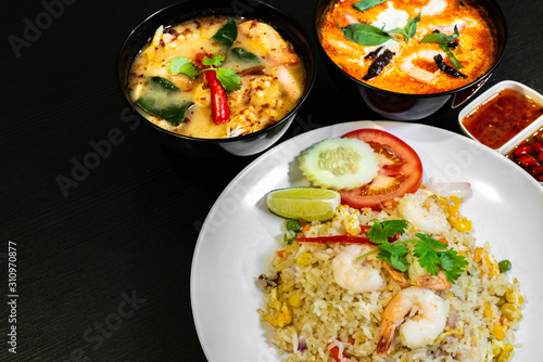 Thai seafood fried rice served with prawns in a white plate  and two bowls of Tom Yum Soup in the background.