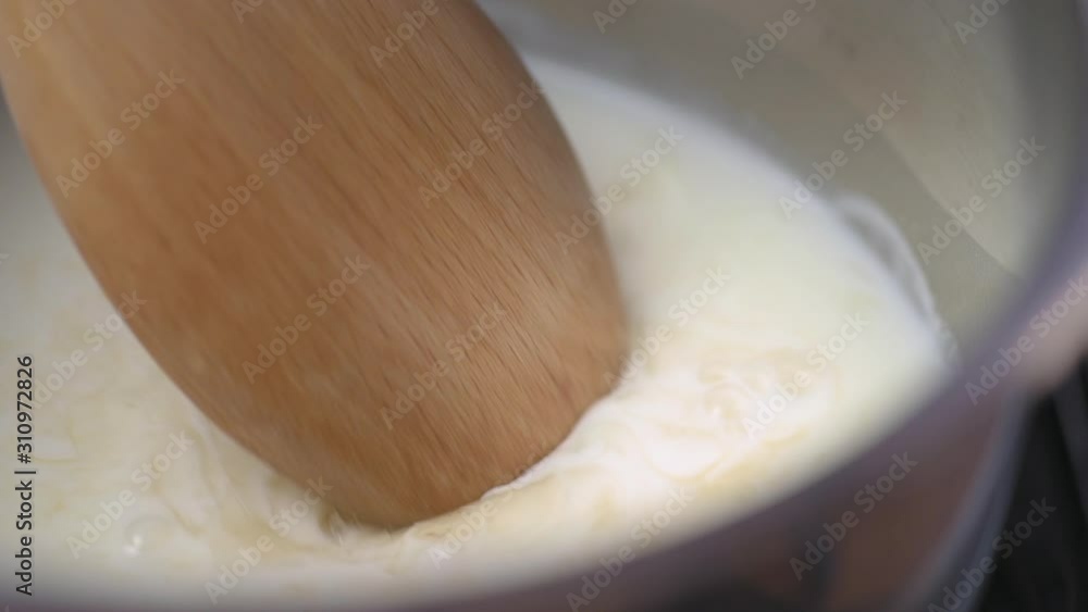 Putting gelatine into pot of milk and stir with a wooden spoon close up. Putting gelatine into pot of milk and stir with a wooden spoon close up.