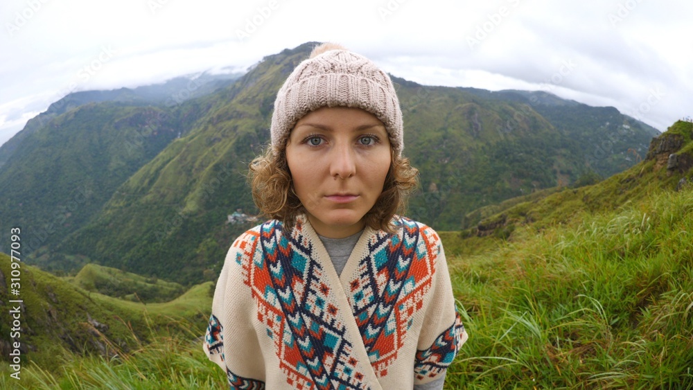 Portrait Of Young Hiker Woman In Mountains Wearing Poncho And Hat