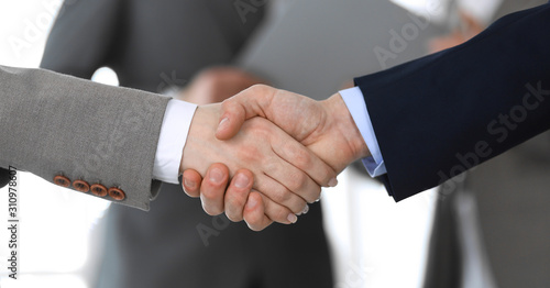 Business people shaking hands while standing with colleagues after meeting or negotiation, close-up. Group of unknown businessmen and women in modern office. Teamwork, partnership and handshake