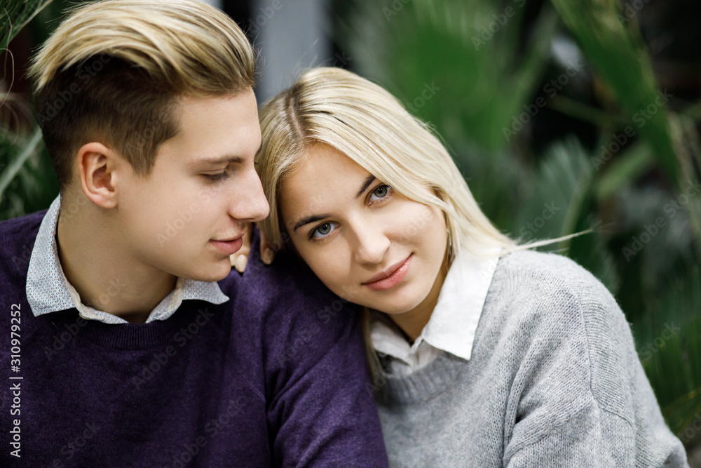 Cute blond guy and girl sitting among tropical plants in big store. Shop for decor Cute blond guy and girl sitting among tropical plants in big store. Shop for decor