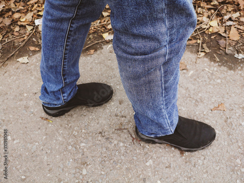 The legs of a man in jeans and shoes are on the road
