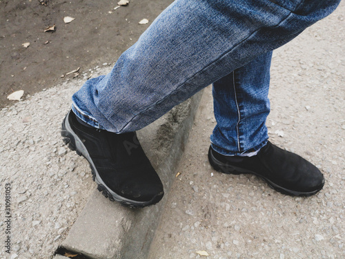 The legs of a man in jeans and shoes are on the road