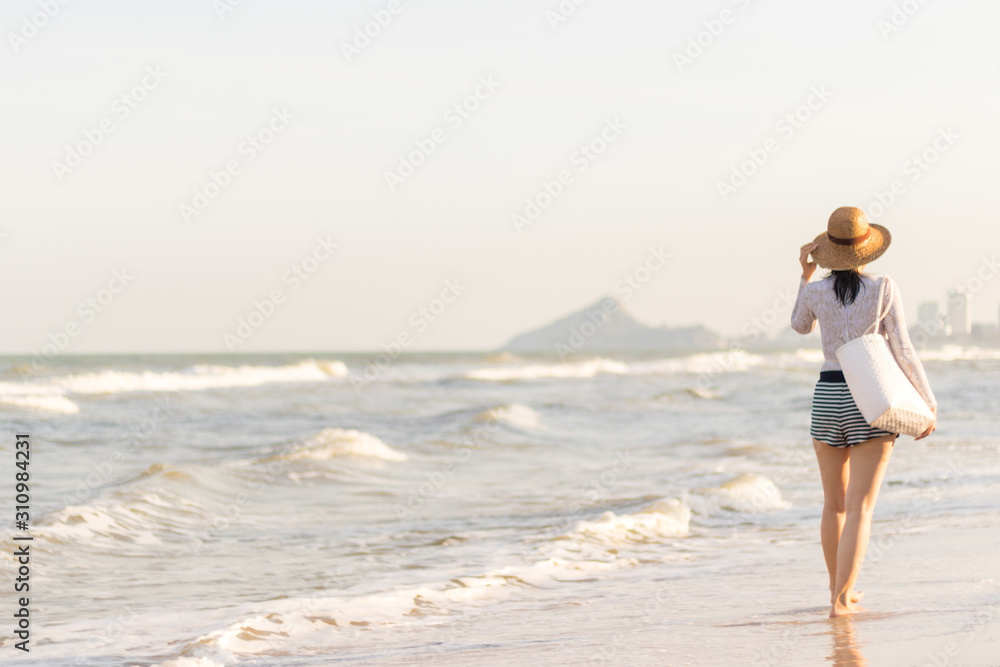 An asian woman wearing panama hat and sunglasses, happy girl walking along the beach in summer time,