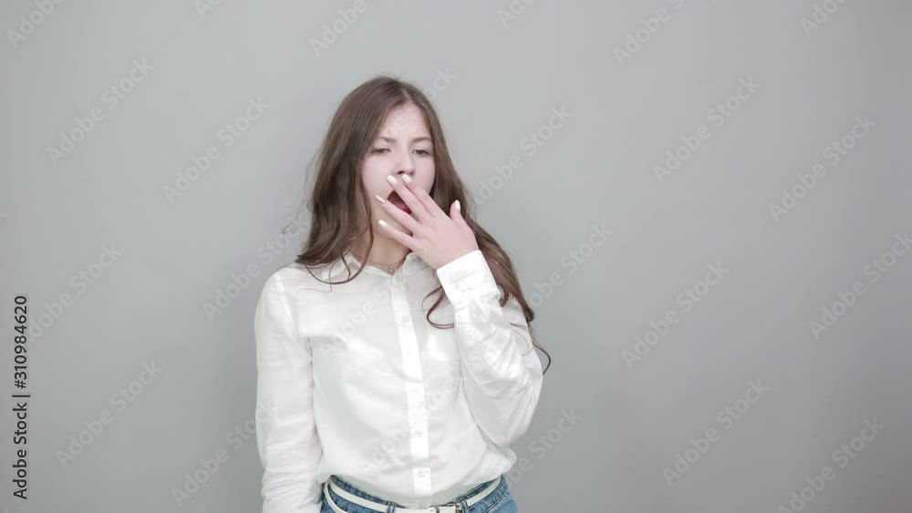 Boring young woman in fashion white shirt isolated on gray background in studio yawning, holding hand on mouth, sleepy. People sincere emotions, lifestyle concept. Boring young woman in fashion white shirt isolated on gray background in studio yawning, holding hand on mouth, sleepy. People sincere emotions, lifestyle concept.