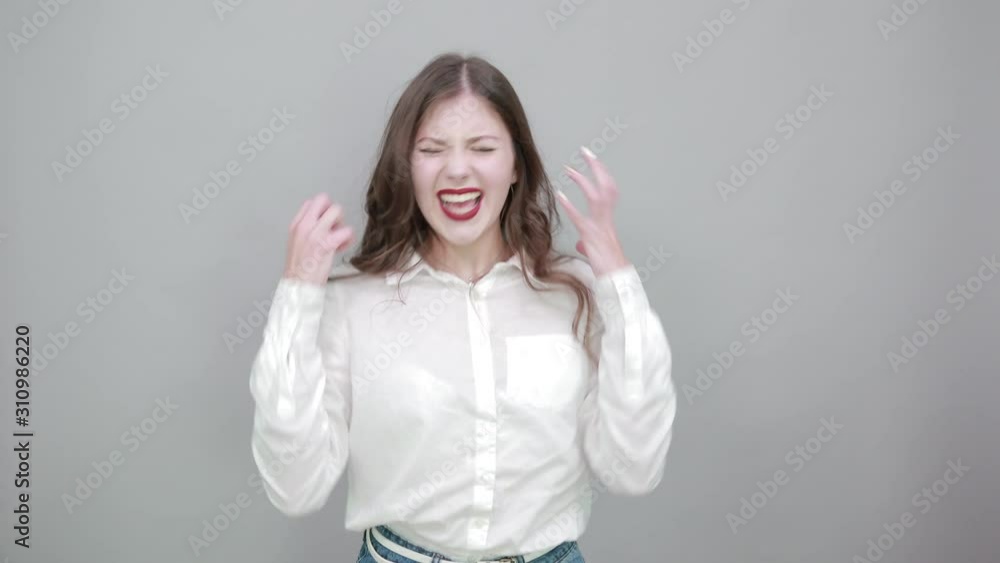 Attractive young brunette woman over isolated gray background wearing casual white shirt, sprads hands, doing winner gesture. People lifestyle concepte.