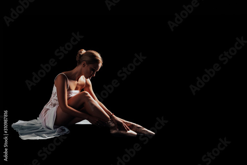 Graceful ballet or gymnast sitting on a black background wears shoes - pointe shoes. dancer in a white dress. Isolated. Dancer posing in Studio with copy space. black background 