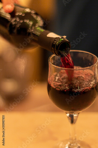 The bartender pours red wine from the bottle into a glass.