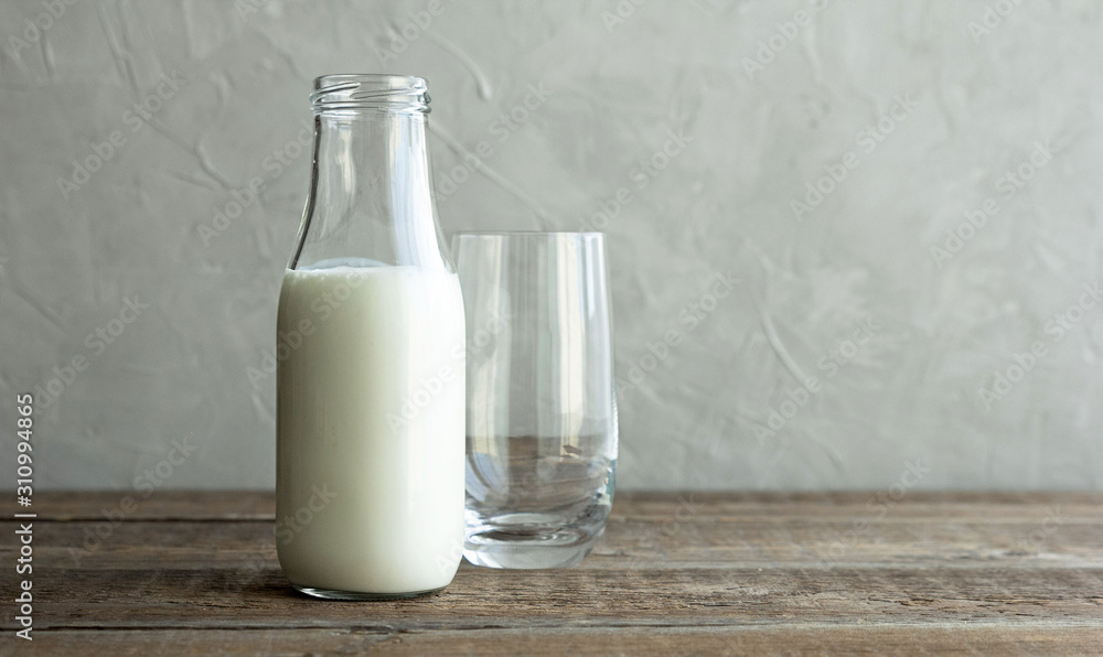 A glass bottle with kefir, milk or homemade fresh yogurt stands on a rustic table and next to it is an empty glass cup. Kefir is a healthy snack and it is rich in prebiotics. A glass bottle with kefir, milk or homemade fresh yogurt stands on a rustic table and next to it is an empty glass cup. Kefir is a healthy snack and it is rich in prebiotics.
