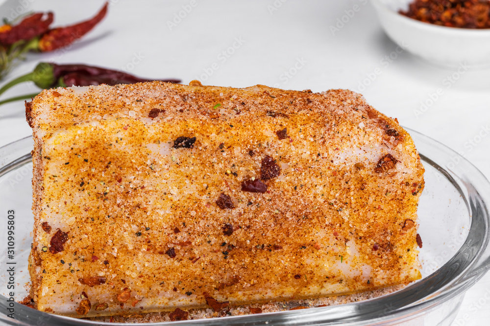A large piece of salted lard with paprika and hot pepper lies in a white plate on a white background A large piece of salted lard with paprika and hot pepper lies in a white plate on a white background