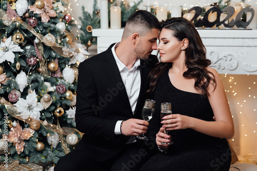 Loving couple, is stylishly dressed near a Christmas tree. Christmas time. Christmas mood. Loving couple celebrating New Year and Christmas with champagne. A bearded guy with a girl pose in a studio 