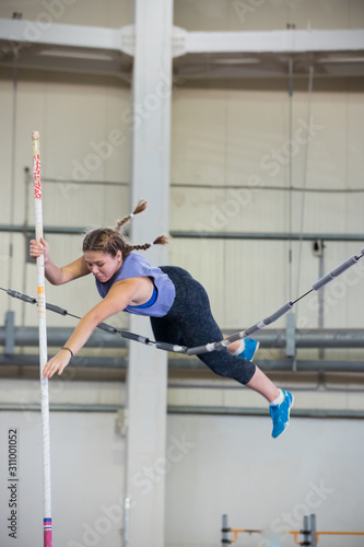 Pole vaulting indoors - young woman with pigtails jumping over the partition trying not to touching it