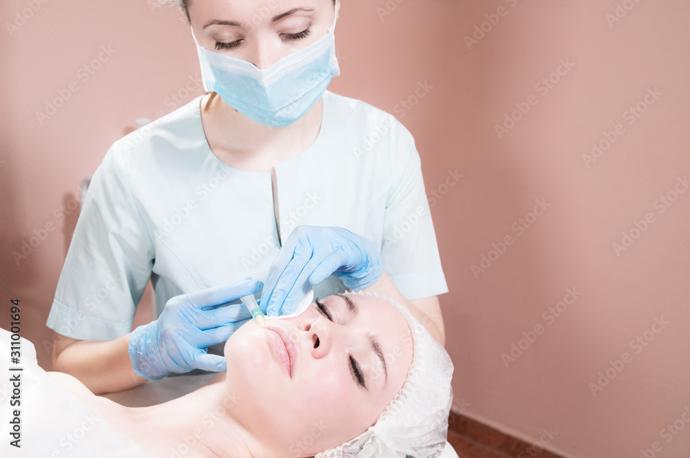 Close-up Attractive young woman gets anti-aging face injections. She lies calmly in a clinic or salon. An experienced young cosmetologist fills female wrinkles with hyaluronic acid from a syringe