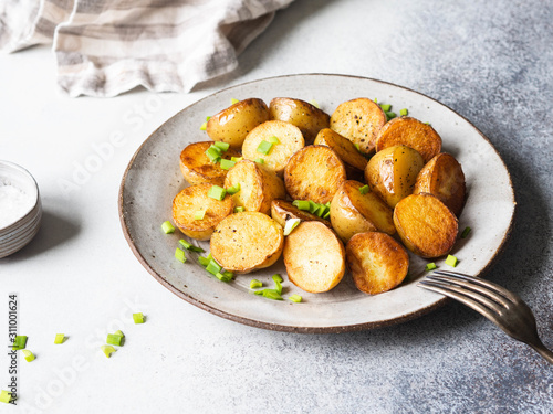 Fried roasted potato wedges with scallions on vintage plate on a gray background